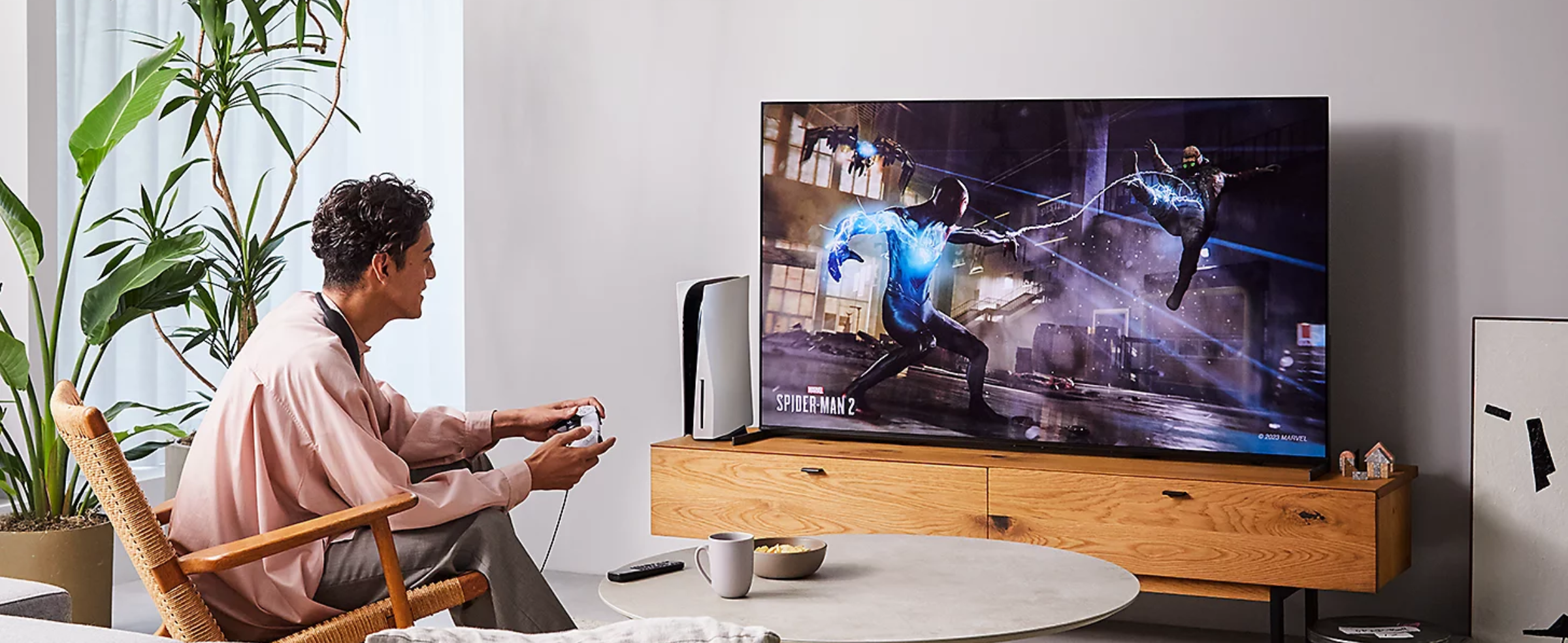 Person sitting on a chair in a living room wearing BRAVIA Theatre U while playing a game on a big screen TV with screenshot of a Spider-Man 2 street scene 