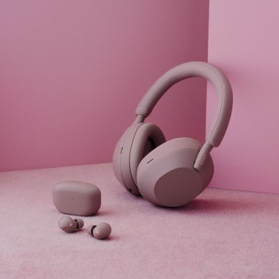 Sony headphones and a pair of Sony earbuds. The headphones are on a pink surface, while the earbuds are in a small case next to them. The headphones and earbuds are a dusty pink color.